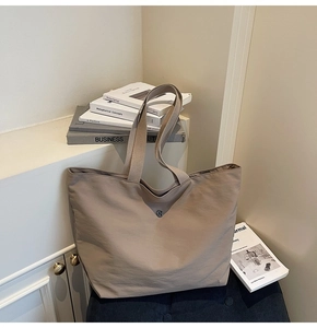 Detalle de bolso tote grande de lona con logo metálico en un entorno minimalista