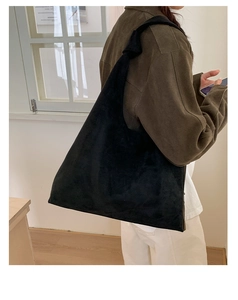 Close-up of black suede tote bag with knotted shoulder strap detail on a female model