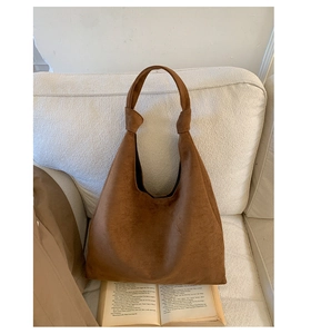 Detailed close-up of brown suede tote bag with stylish knot strap on a sofa background