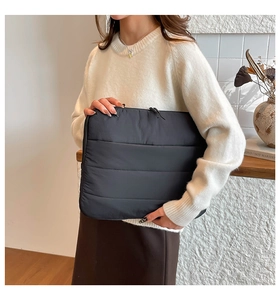 Detail view of a black quilted laptop sleeve with dual zippers held in a stylish setting