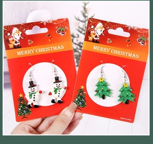 Détail de boucles d'oreilles bonhomme de neige et sapin de Noël sur une carte de voeux rouge