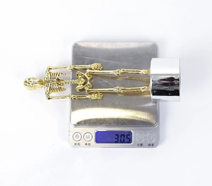 Detailed close-up of a 30.5g golden skeleton figurine on a digital weighing scale