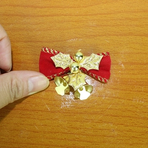 Detail von roter Samtschleife mit goldenen Stechpalmenblättern und kleinen Glocken
