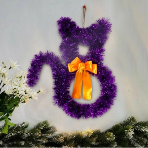 Close-up of a purple tinsel cat wreath with an orange bow for Halloween door decoration