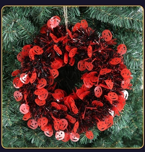 Detailed view of red and black tinsel Halloween wreath with pumpkin cutouts on green tree