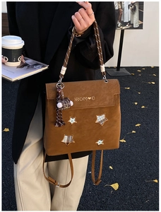 Detailed view of brown matte backpack with star patches and woven handle in autumn setting