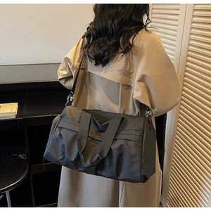 Detailansicht der schwarzen Reisetasche mit verstellbarem Gurt getragen zum Trenchcoat