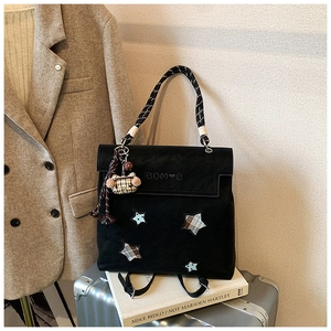 Detail of matte black backpack with star patches, woven rope handle and bear pendant