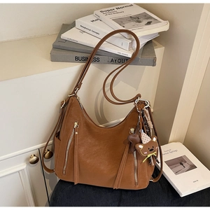 Détail de sac à bandoulière marron avec poches zippées verticales et pompons longs