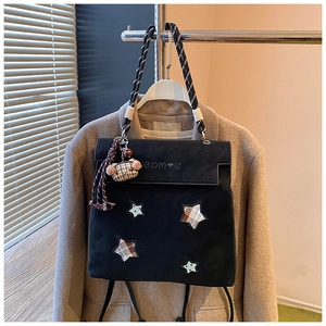 Close-up of black matte backpack featuring star patches, rope handles and a bear pendant