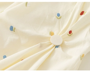 Close-up of cream dress fabric with colorful flower embroidery and a covered fabric button