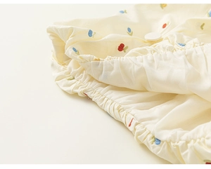 Detailed view of red and blue cherry embroidery on breathable off-white cotton fabric