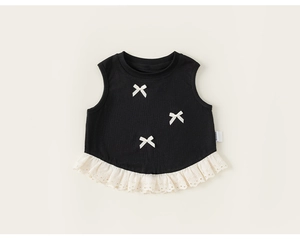 Dettaglio del gilet in maglia nera per neonata con tre fiocchi bianchi e pizzo sul bordo