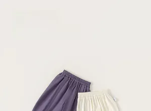 Detail of loose-fit purple and beige cotton pants with elastic waist and side label