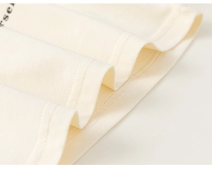 Close-up of fine needlework and double-stitched hem on cream cotton knit t-shirt