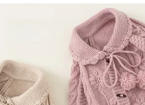 Close-up of cable knit cardigan with floral embroidery and delicate pom-pom ties