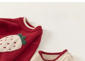 Detail of red strawberry knit pattern and ribbed crew neck on girls' winter sweater