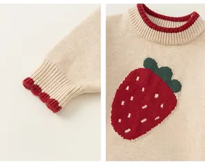 Detailed view of the strawberry embroidery and striped cuffs on a beige knit sweater