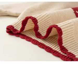 Close-up of cream knit sweater hem with red scalloped trim and soft textured finish