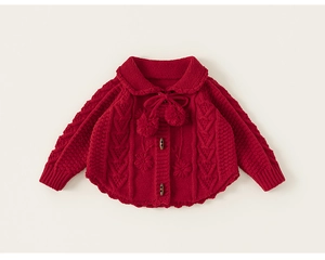 Detail shot of red knit sweater with floral embroidery, pom-poms, and wooden buttons
