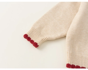 Close-up of beige knit sweater featuring ribbed cuffs and decorative red scalloped edges