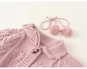 Detail of pink knitted cardigan featuring 3D floral textures and retro wooden toggles