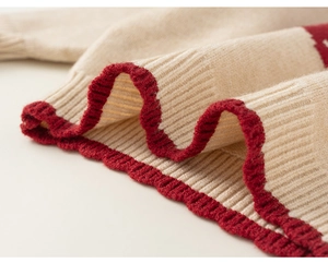 Detail of red wavy ribbed edge on a beige knitted kids sweater with warm texture
