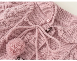 Close-up of pink knit cardigan featuring embossed flowers, pom-poms, and wooden buttons