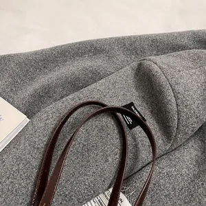 Detail of wool fabric texture and brown leather handle on the gray pillow shoulder bag