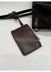 Detail of a chocolate brown mini zipper pouch accessory on a minimalist leather tote bag