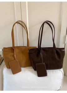 Detail view of suede leather tote bags in tan and dark brown colors on a white sofa