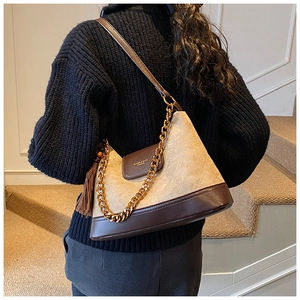 Détail du sac hobo en daim beige avec surpiqûres losanges, chaîne dorée et pompon