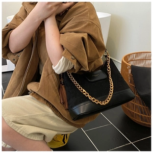 Détail d'un sac en daim noir avec bandoulière en chaîne dorée et gland en cuir