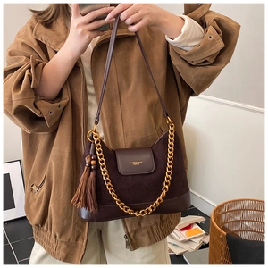 Détail du sac bandoulière en daim marron foncé avec chaîne dorée et gland en cuir élégant