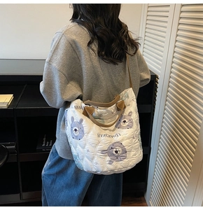 Detail view of white quilted shoulder bag with bear pattern and brown straps on model