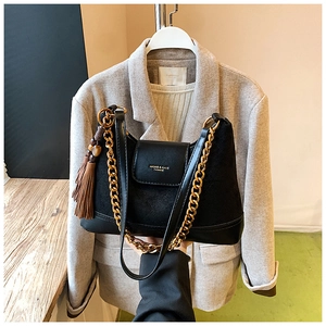 Détail du sac en daim noir avec chaîne dorée, pompon décoratif et logo embossé