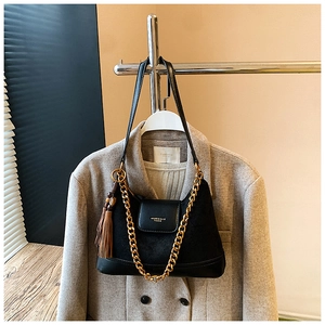 Détail d'un sac en daim noir avec chaîne dorée, bandoulière en cuir et pompon décoratif