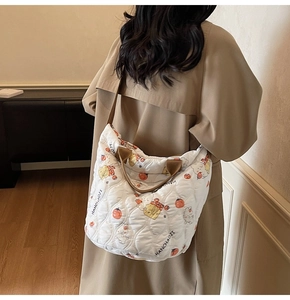 Detail of white quilted tote bag featuring cartoon fruit prints and broad brown strap