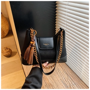 Détail du sac matelassé en daim noir avec chaîne dorée et breloque à pompon élégante