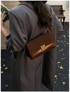 Détail d'un sac à bandoulière en cuir marron avec un fermoir doré porté par un mannequin