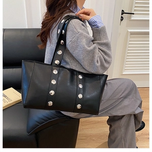 Detalle de bolso tote negro de cuero con remaches plateados y correa ancha para el hombro