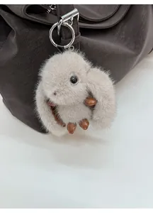 Close-up of a plush rabbit charm with leather limbs hanging on a brown tote bag