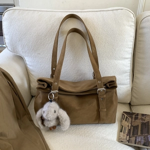 Brown leather tote bag featuring silver buckles and cute rabbit plush charm on a sofa