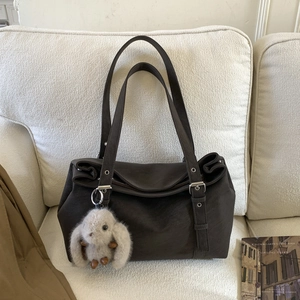 Detail of dark brown tote bag with plush bunny charm and long straps on a sofa