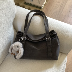 Detail of dark brown faux leather tote bag with plush bunny charm on white sofa