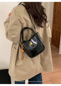 Retro glänzende schwarze Handtasche mit dekorativem Holzperlen-Anhänger an der Schulter