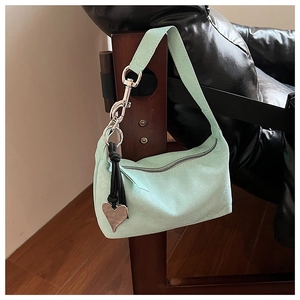 Détail du sac oreiller en daim vert menthe avec pendentif coeur sur une chaise en bois