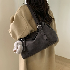 Detail view of large brown suede tote bag with silver buckle and plush bird charm on shoulder