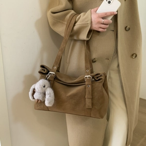 Detail of a brown suede shoulder bag with dual strap buckles and a cute rabbit pendant
