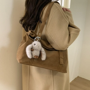 Detail of a brown matte suede tote bag with a cute white bunny plush keychain charm